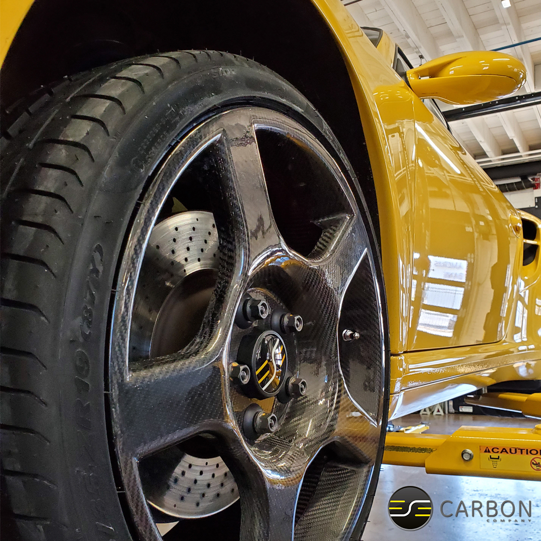 a yellow car on a lift with a carbon fiber wheel